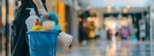 Profissional de limpeza comercial segurando balde com produtos e equipamentos de limpeza em um shopping