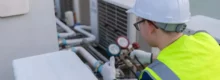 Técnico com capacete e colete verifica manômetros de ar-condicionado, seguindo PMOC