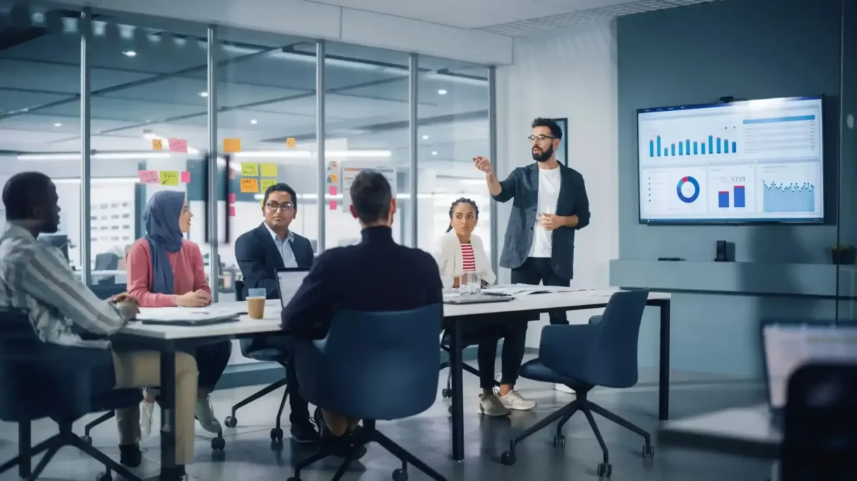 Profissional apresenta dados em reunião corporativa, destacando atividade-fim com gráficos em tela