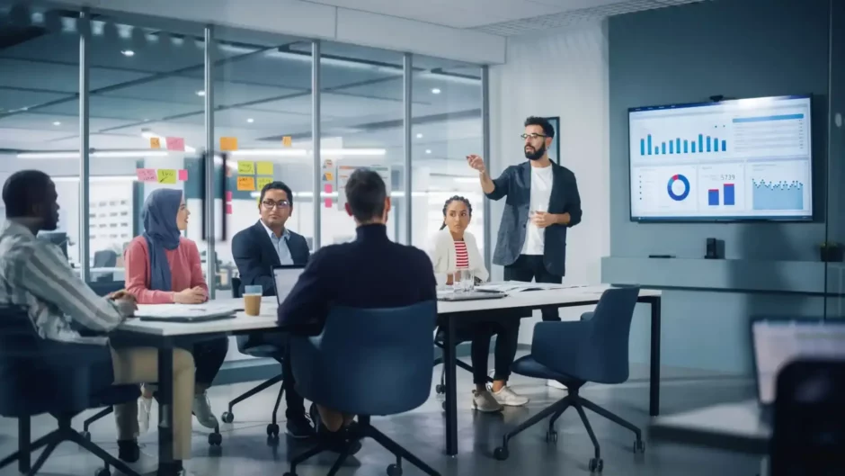 Profissional apresenta dados em reunião corporativa, destacando atividade-fim com gráficos em tela