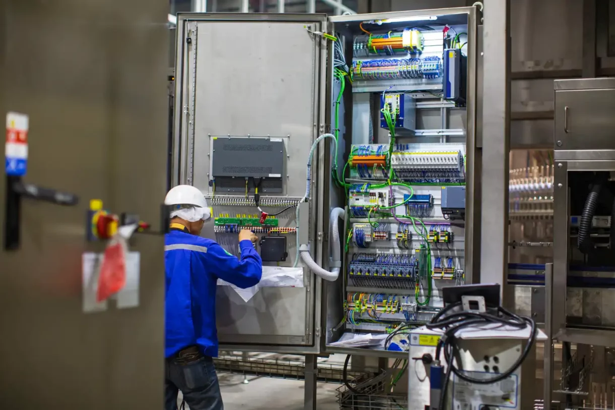 Técnico realiza manutenção em painel de controle de cabos e conexões industriais, representando infraestrutura elétrica organizada e segura