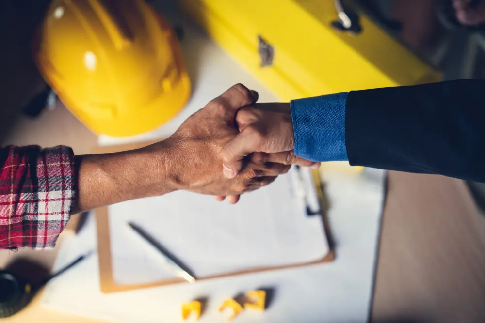 Acordo SLA Aperto de mãos entre dois profissionais da construção civil selando acordo SLA com capacete ao fundo