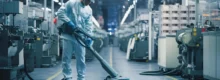 Operário realizando aspiração industrial em piso de fábrica com equipamento especializado